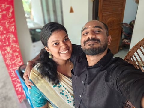 Sneha in a cream kasavu saree and Hari with chandanam on their foreheads, on a veranda