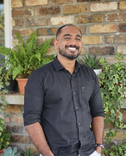 Hari in a black shirt against a brick wall, smiling