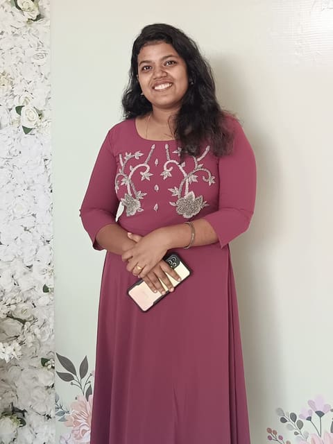 Sneha in a maroon embroidered gown against a white floral wall