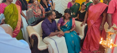 Hari and Sneha exchanging rings on a sofa, both laughing, family gathered around and the nilavilakku lit